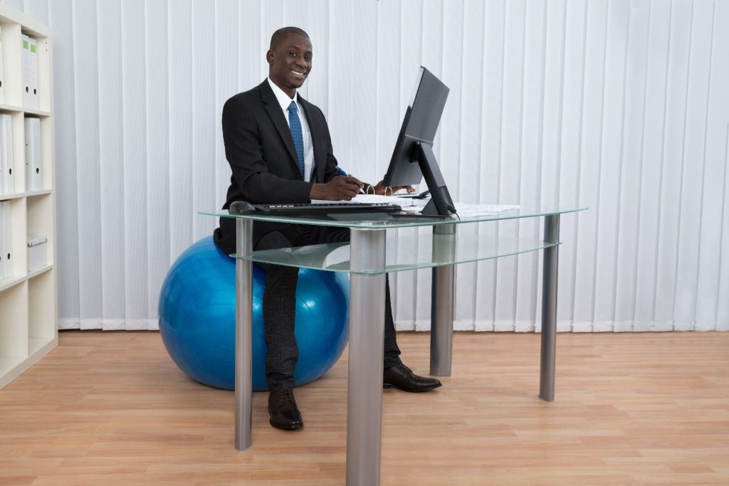 A businessman sits on a ball at his desk