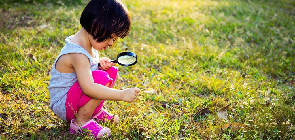 Girl exploring outdoors with magnifying glass