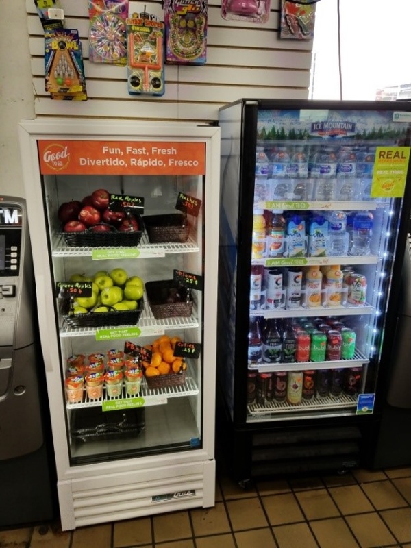 The Healthy Corner Store conversion after with a cooler of fruit and a beverage cooler full of water, seltzer, and other healthy beverages