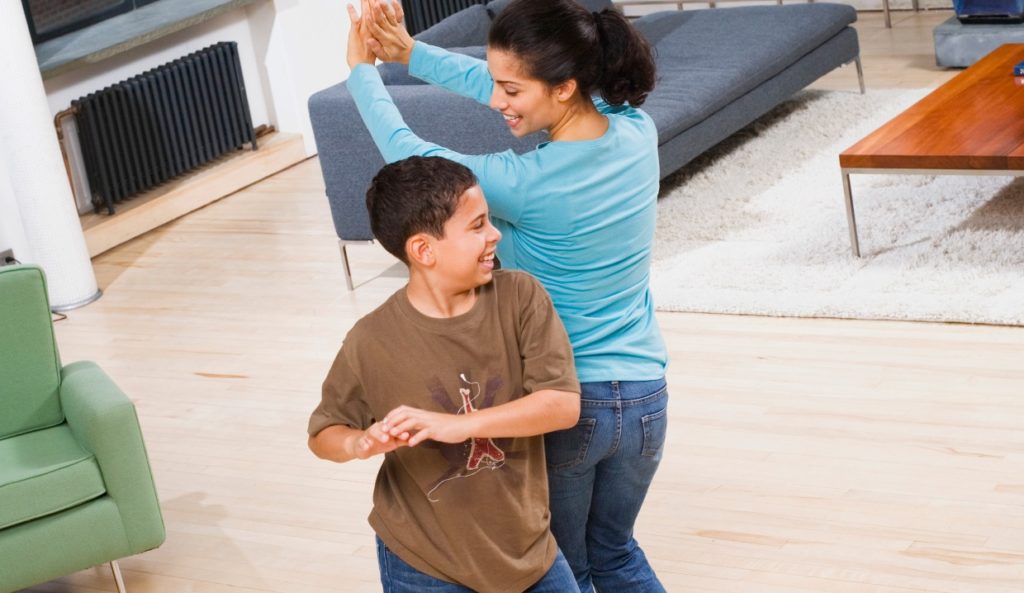 A mom and son dance in the living room
