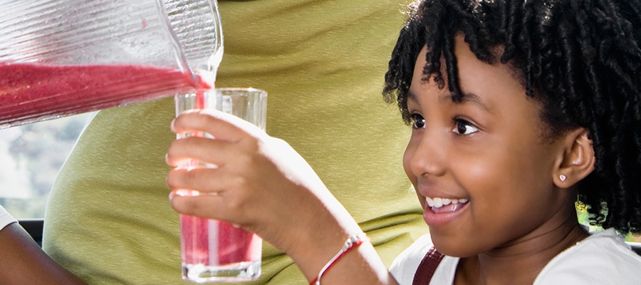 A young girl holds a glass while a fruit smoothie is poured in