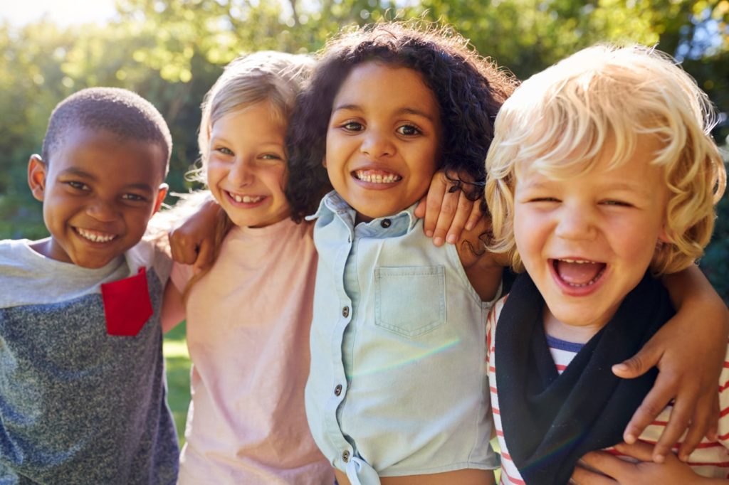 Four young children smile with their arms around one another