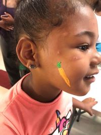 A young girl gets some face paint -  a carrot painted on her cheek