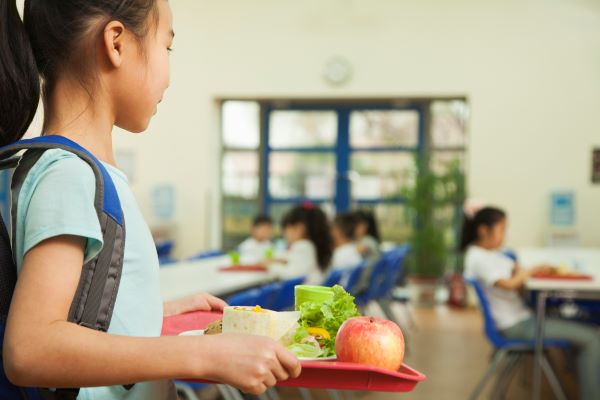 Elementary school girl carries a tray with a healthy lunch