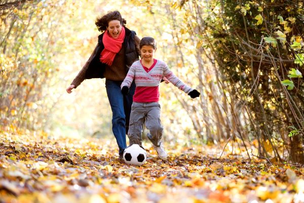 Mom and daughter kick a soccer ball in the woods