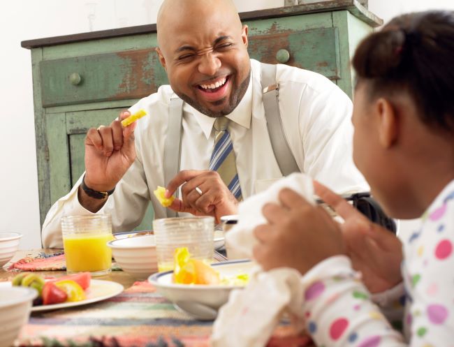 Dad laughs eating breakfast with daughter